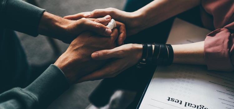 Psychotherapist with clipboard and pen consults fraught woman making closed gestures while sitting on comfortable couch in clinic office close view